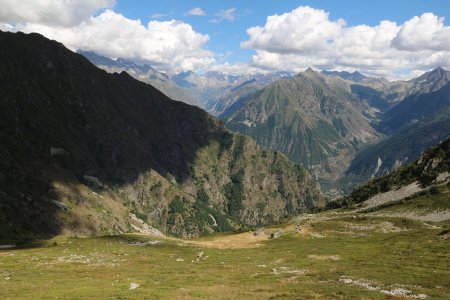 En s’élevant au-dessus des cabanes et de l’alpage.