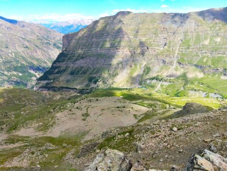 Droit devant, l’on aperçoit le toit de la Grande Cabane de Faravel. Descendre en visant la gauche du vaste pierrier ovale